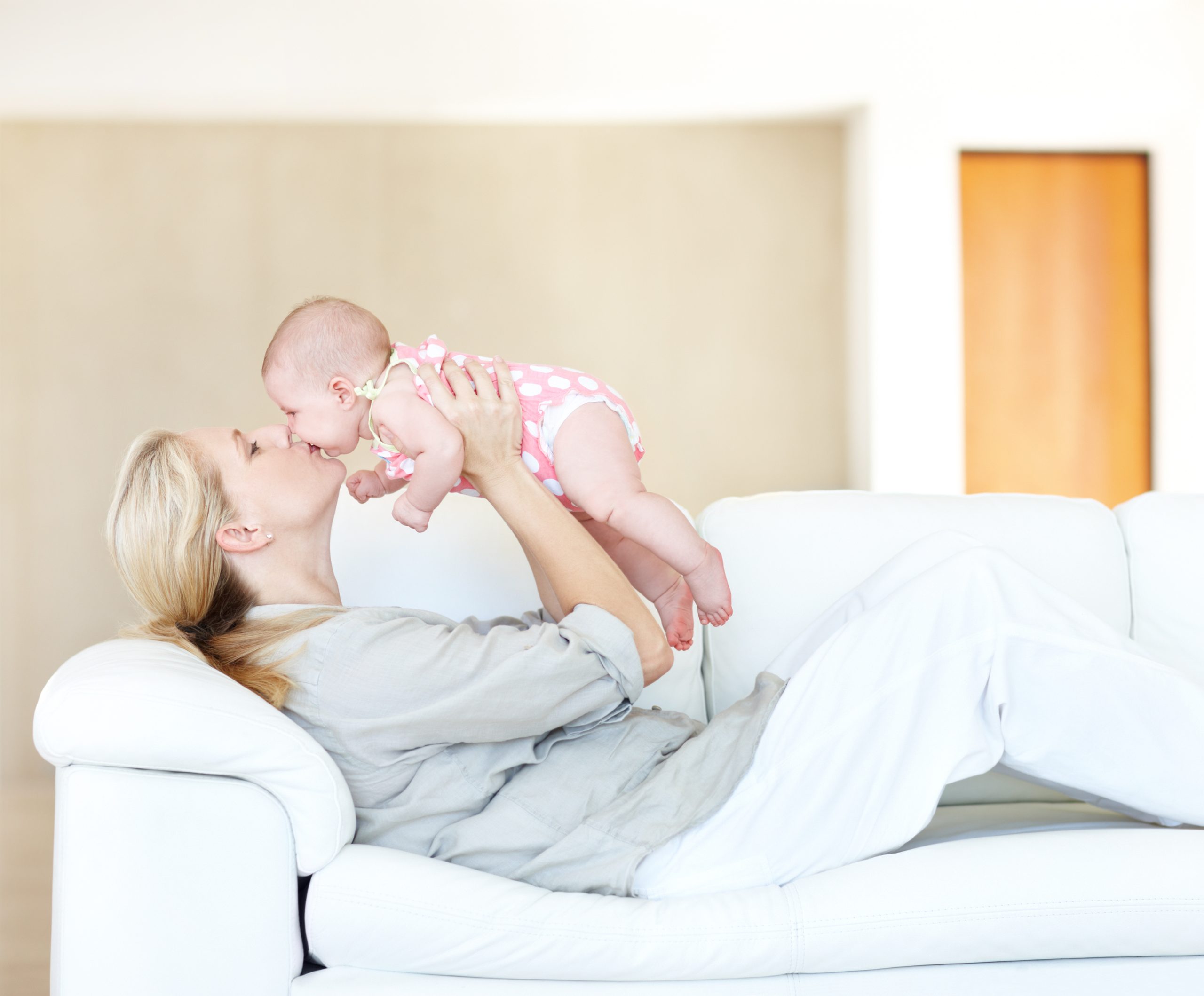 Thankful mother giving her cherubic newborn a loving kiss upon the lips relaxing on sofa